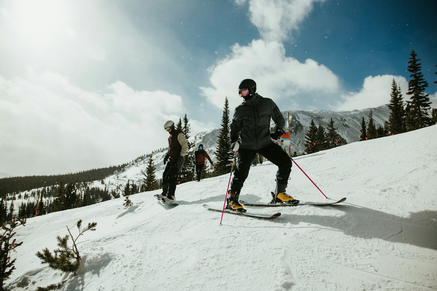 Trzy osoby jeżdżą na nartach i snowboardzie po zaśnieżonej górze.